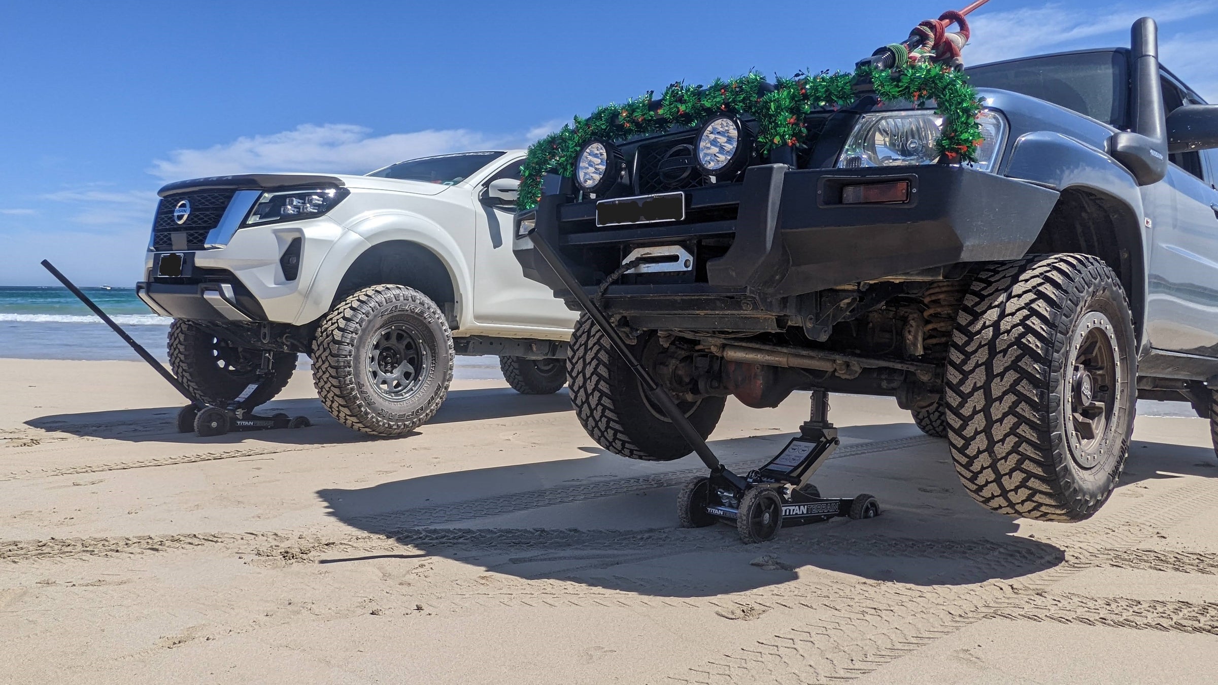 two utes being lifted by 2 titan terrain rugged floor jacks on sand